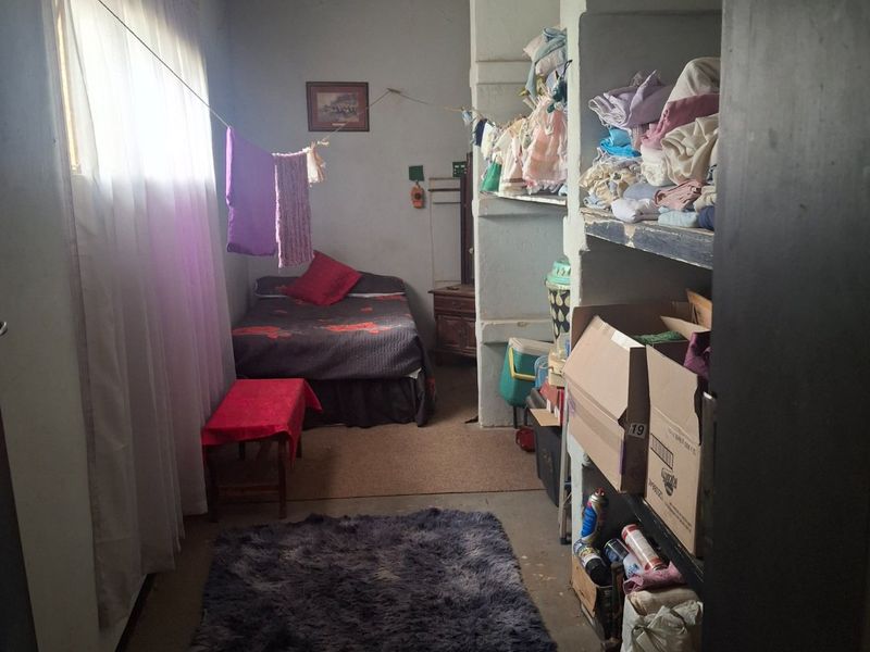 A small bedroom featuring built-in shelving units and a window with curtains, requiring cosmetic updates and maintenance to improve the overall condition.