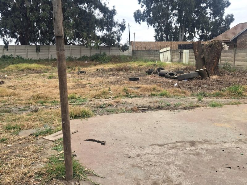 A large, undeveloped rear yard area featuring a concrete slab, perimeter precast concrete walling, and significant overgrown vegetation requiring clearing.