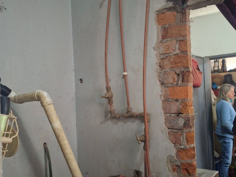 Utility area featuring exposed copper plumbing and unfinished brickwork, requiring significant renovation and finishing to be functional.