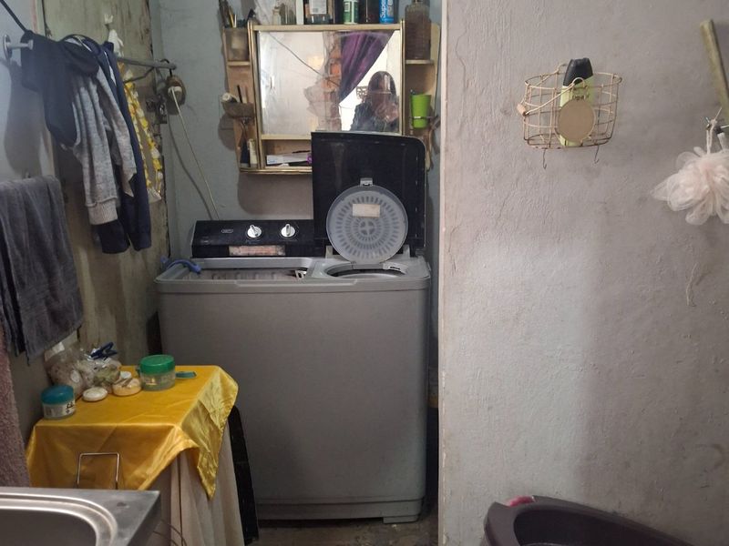 A functional laundry area featuring a sink and space for washing equipment, requiring maintenance and cosmetic updates to improve the overall condition.