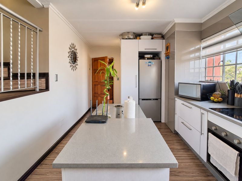 Modern kitchen featuring a central island with quartz countertops, sleek white cabinetry, built-in oven, and durable laminate flooring.