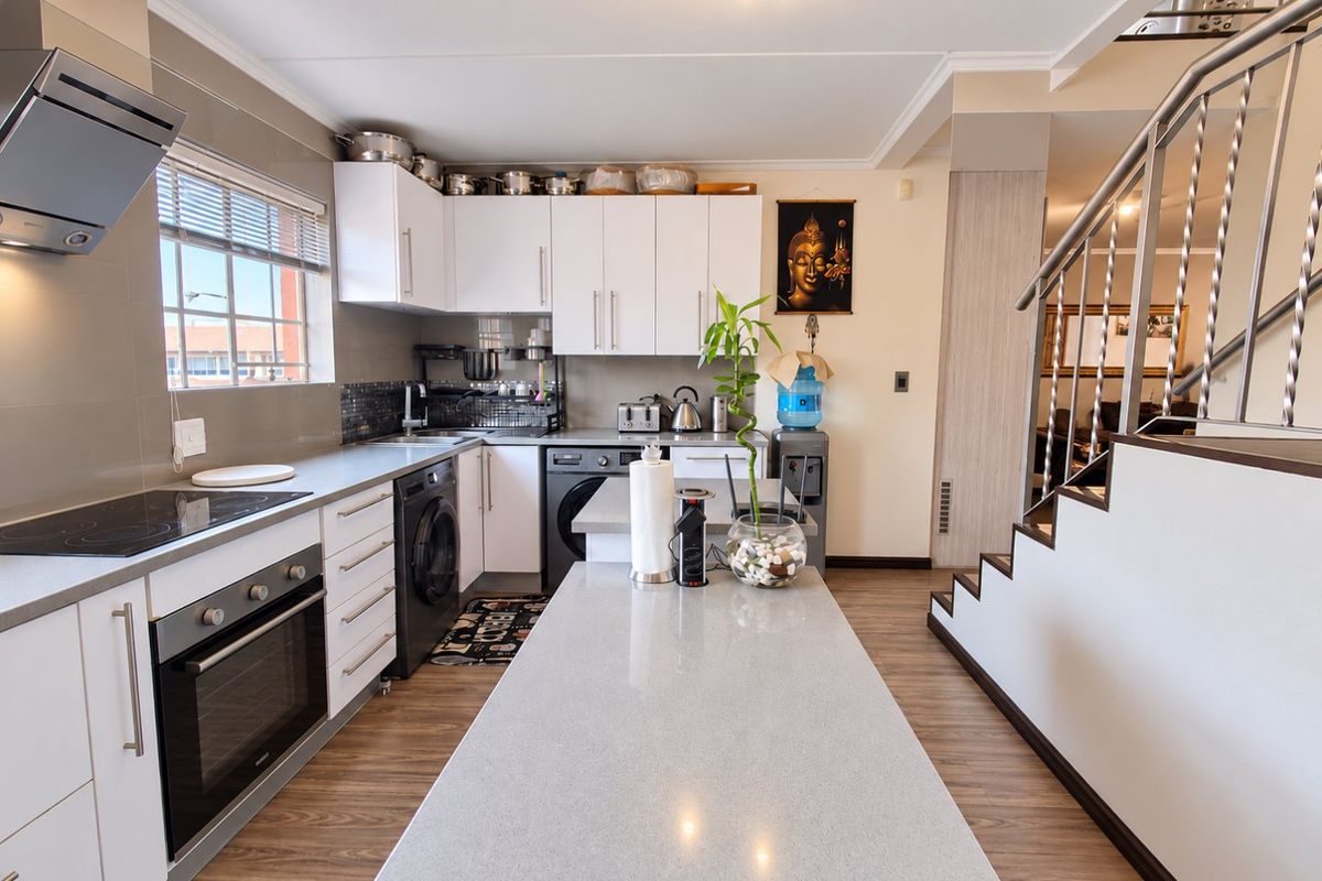 Modern kitchen featuring white cabinetry, stone-topped island, built-in oven, electric cooktop, and integrated laundry appliances, adjacent to an open staircase.