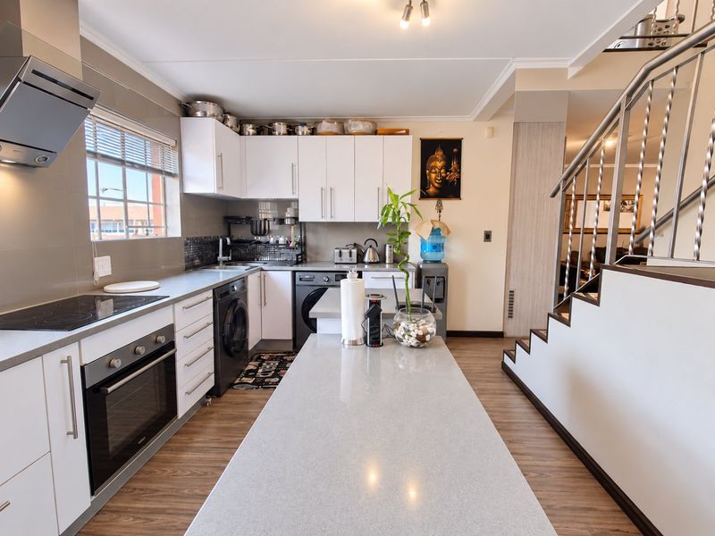 Modern kitchen featuring white cabinetry, stone-topped island, built-in oven, electric cooktop, and integrated laundry appliances, adjacent to an open staircase.