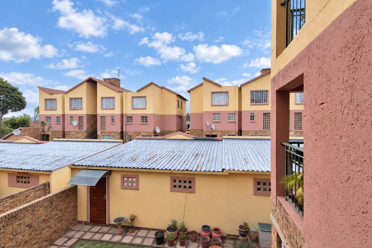 View of the rear exterior of the townhouse complex, featuring paved patio areas, brick boundary walls, and corrugated metal roofing on the lower structures.