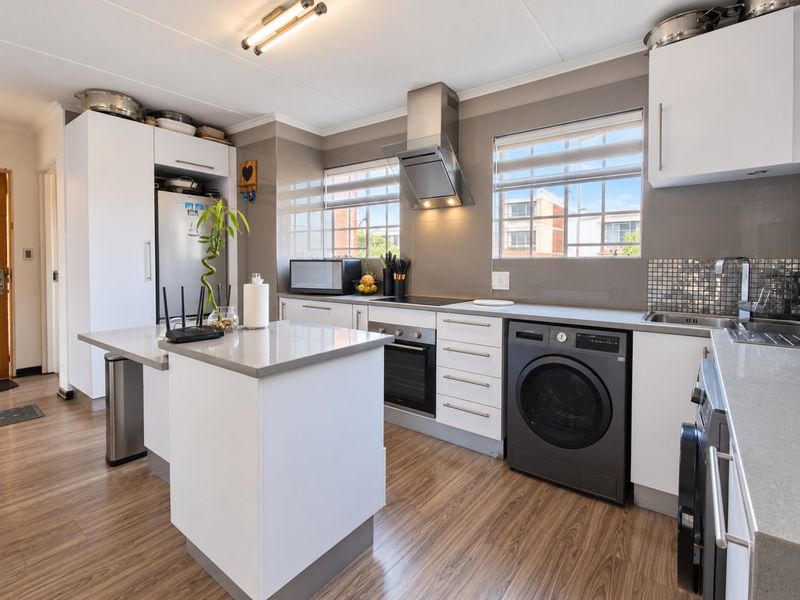 Modern kitchen featuring white cabinetry, stone countertops, stainless steel appliances, and a functional island layout with integrated laundry facilities.
