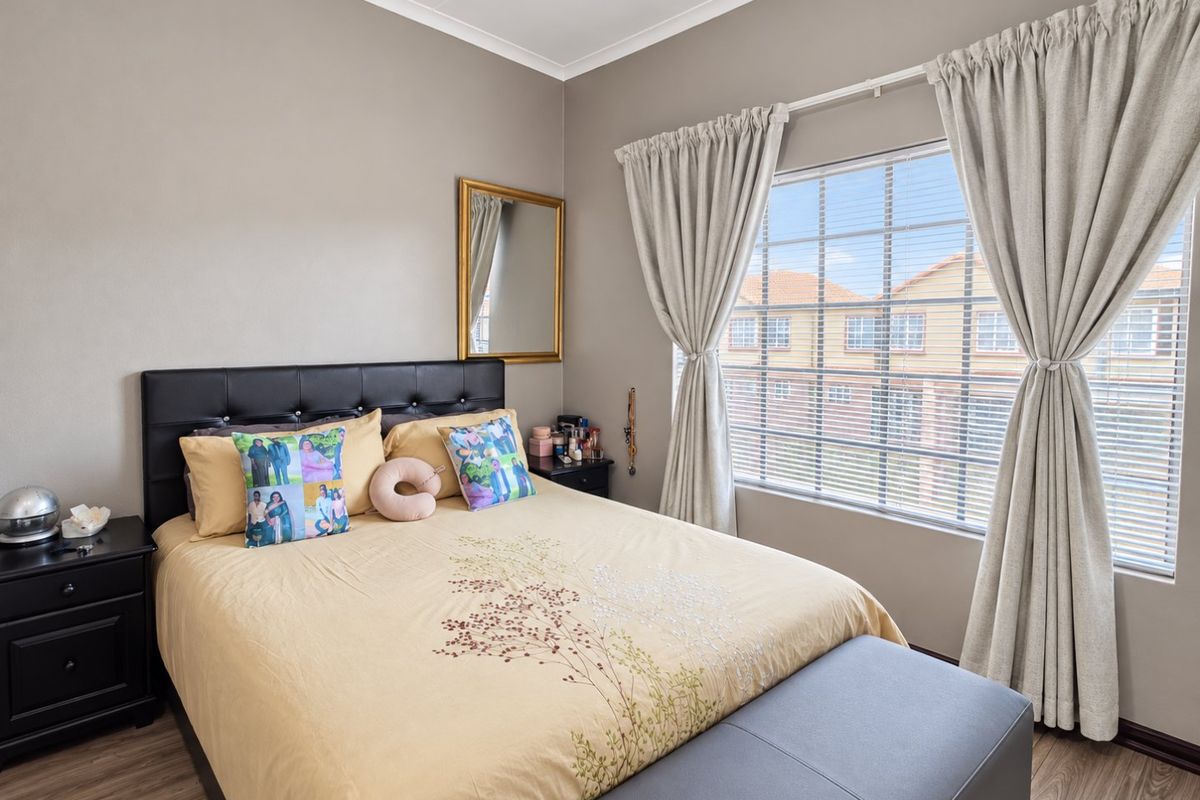 A well-maintained bedroom featuring laminate flooring, neutral wall tones, and a large window with fitted blinds and curtains.