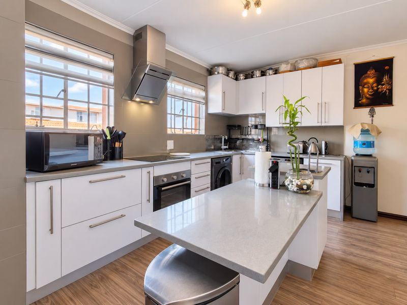 Modern kitchen featuring white cabinetry, stone countertops, a central island, built-in oven, electric hob, and stainless steel extractor fan with laminate flooring.