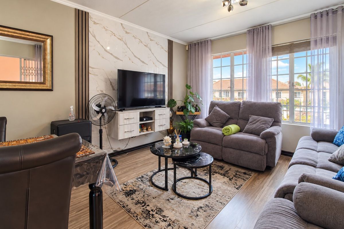 A well-maintained living room featuring laminate flooring, a decorative marble-look feature wall, and large windows providing natural light.