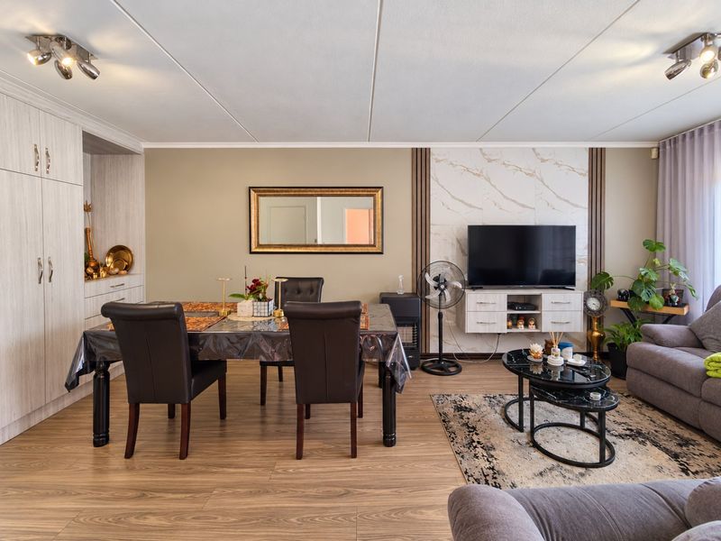 Open-plan living and dining area featuring wood-look laminate flooring, built-in storage cabinetry, and a decorative marble-effect feature wall.