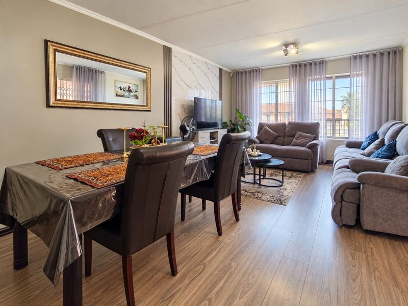 Spacious open-plan living and dining area featuring modern laminate flooring, a decorative marble-look feature wall, and large windows providing ample natural light.