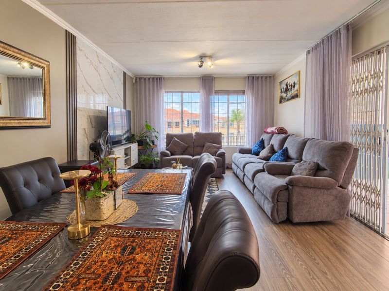 Spacious open-plan living and dining area featuring modern laminate flooring, a marble-look feature wall, and large windows providing ample natural light.