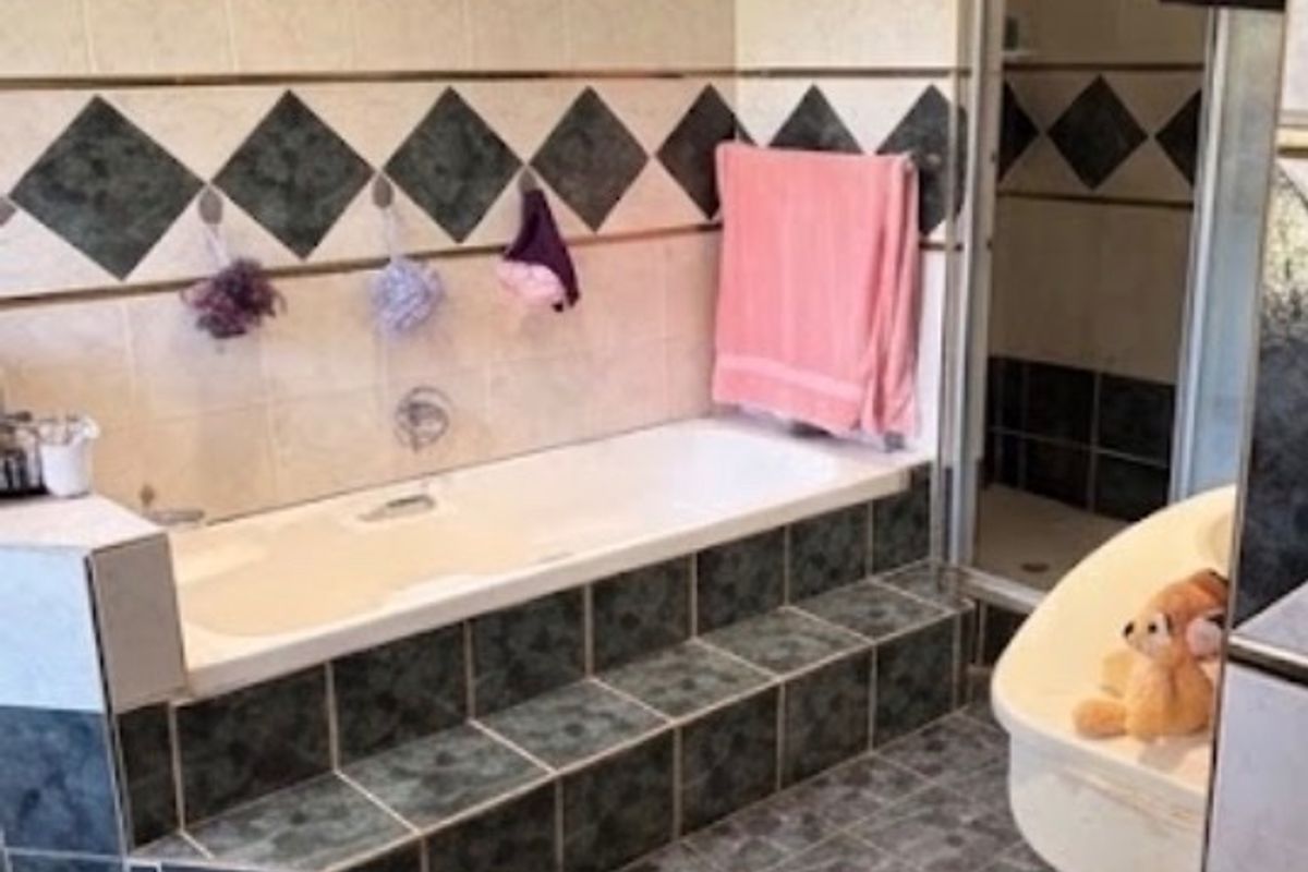 A bathroom featuring a built-in tiled bathtub, a separate shower enclosure, and a vanity basin with dated wall and floor tiling.