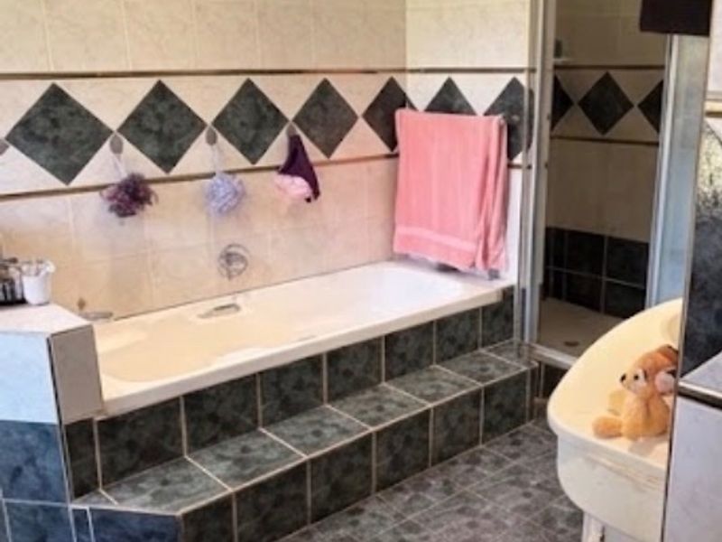 A bathroom featuring a built-in tiled bathtub, a separate shower enclosure, and a vanity basin with dated wall and floor tiling.