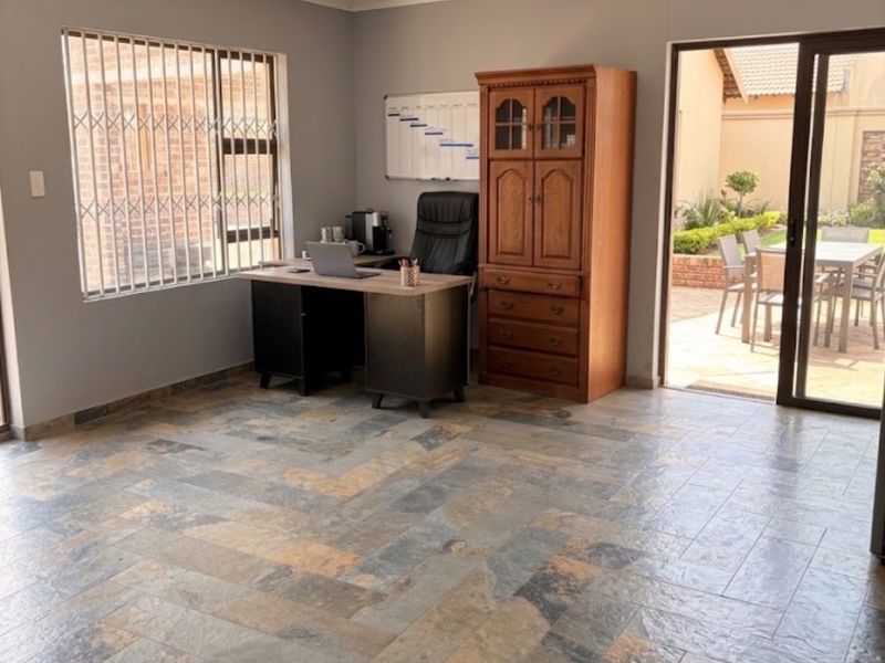 A spacious home office featuring durable slate tile flooring, recessed lighting, and direct access to an outdoor patio area through sliding glass doors.