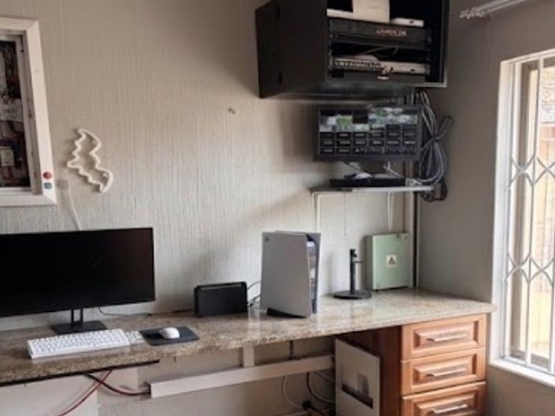 A functional home office space featuring a built-in desk with integrated cabinetry and security bars on the window.