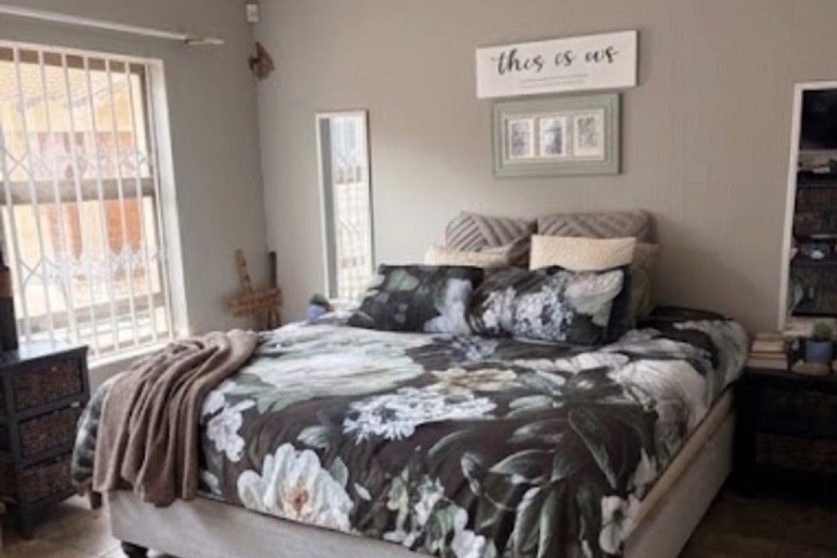 A well-maintained bedroom featuring tiled flooring, neutral wall tones, and security bars on the windows.