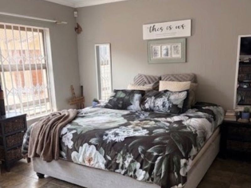 A well-maintained bedroom featuring tiled flooring, neutral wall tones, and security bars on the windows.