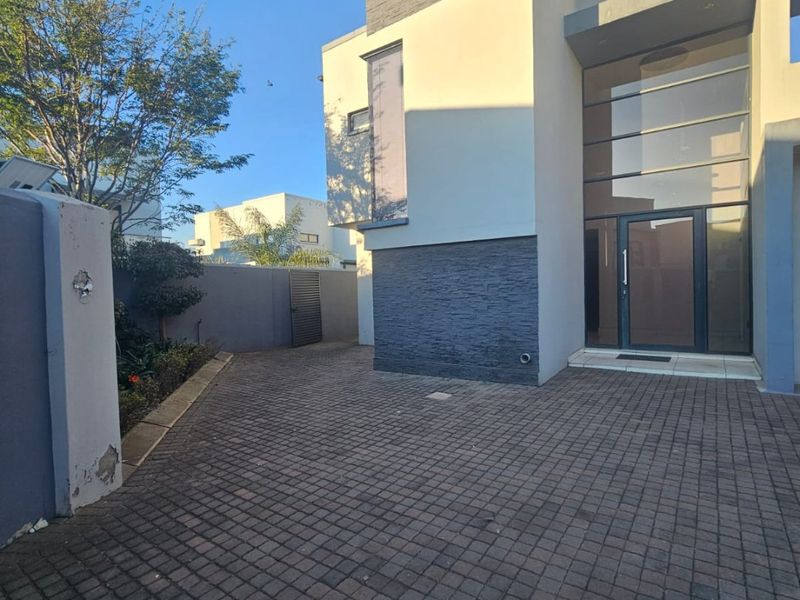 Modern double-storey home entrance featuring stone cladding, a paved driveway, and a striking double-volume glass front door.