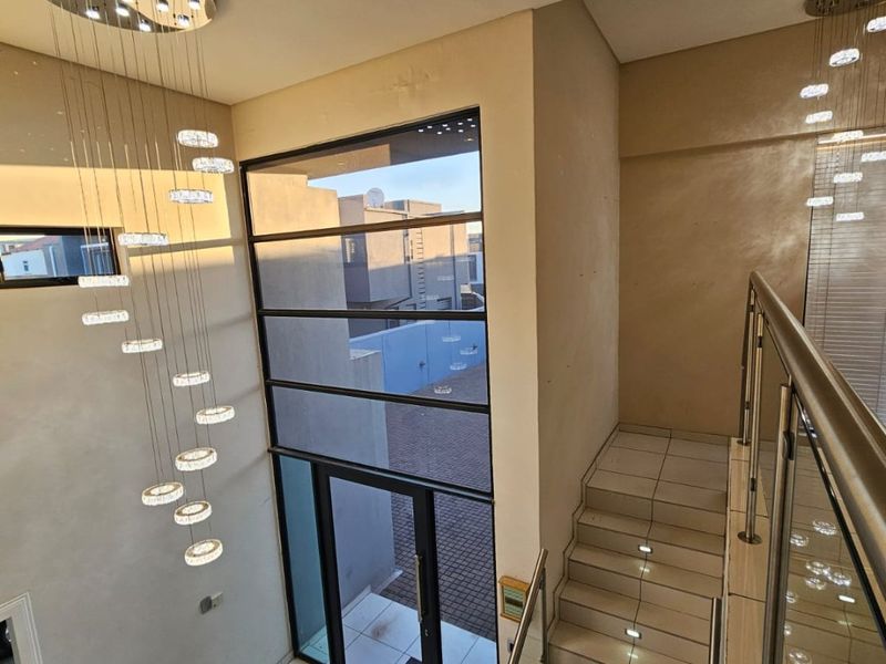 Modern double-volume entrance hall featuring a sleek staircase with glass balustrades, tiled flooring, and striking contemporary pendant lighting.