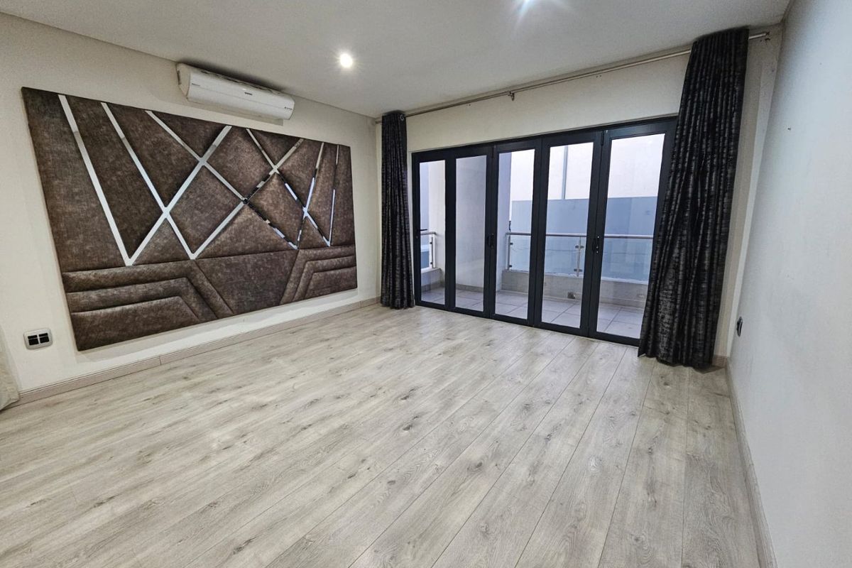 Spacious living area featuring light wood-look laminate flooring, recessed lighting, a wall-mounted air conditioner, and bi-fold doors leading to a private balcony.