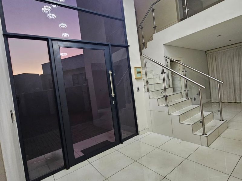 Spacious double-volume entrance hall featuring large glass panels, tiled flooring, and a modern staircase with stainless steel and glass balustrades.