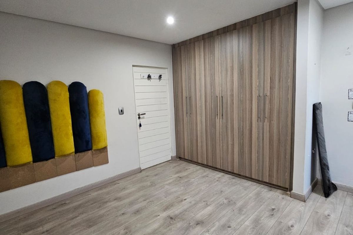 A clean, modern bedroom featuring light wood-look laminate flooring, ample built-in cupboard storage, and recessed ceiling lighting.