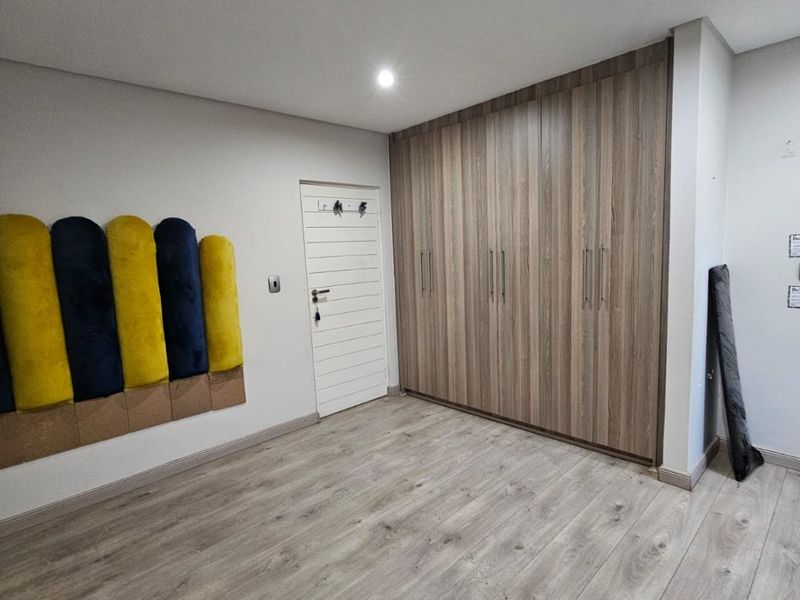 A clean, modern bedroom featuring light wood-look laminate flooring, ample built-in cupboard storage, and recessed ceiling lighting.