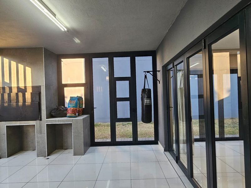A modern covered patio featuring large format floor tiles, a built-in braai, and expansive aluminium stacker doors providing seamless indoor-outdoor flow.