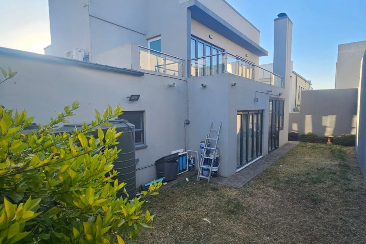 Rear view of a modern double-story house featuring a balcony with glass balustrades, large sliding doors, and a private garden area.
