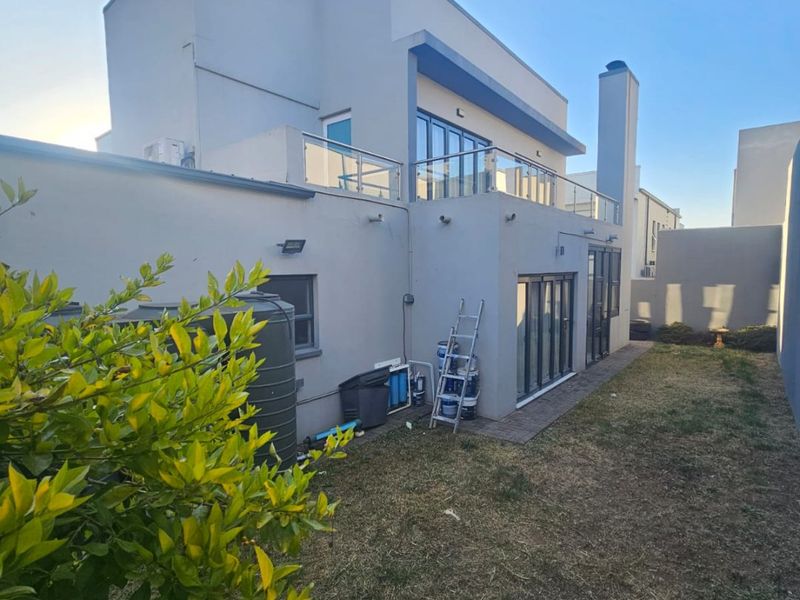 Rear view of a modern double-story house featuring a balcony with glass balustrades, large sliding doors, and a private garden area.