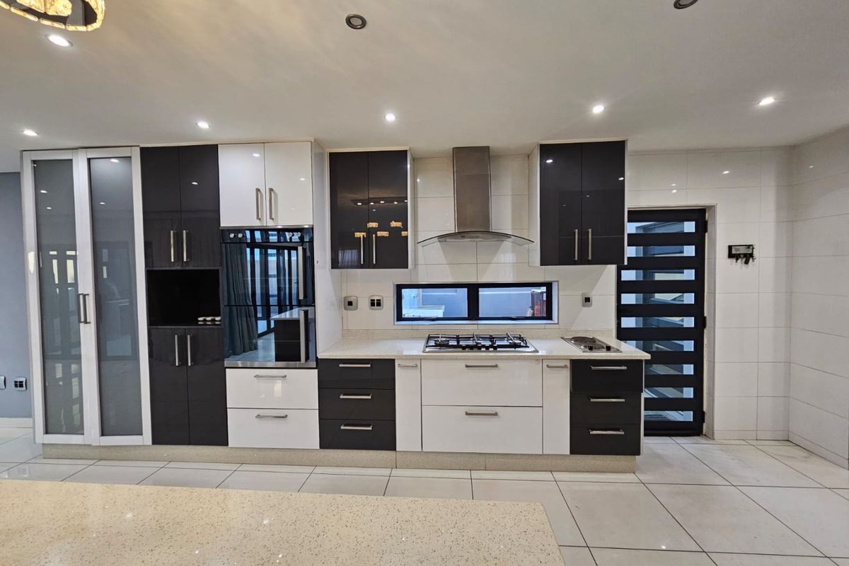 Modern kitchen featuring high-gloss cabinetry, stone countertops, integrated gas hob, extractor fan, and built-in oven with sleek tiled flooring.
