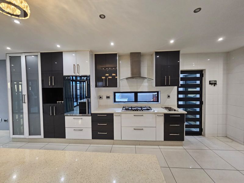 Modern kitchen featuring high-gloss cabinetry, stone countertops, integrated gas hob, extractor fan, and built-in oven with sleek tiled flooring.