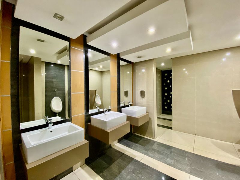 Modern commercial bathroom featuring dual wall-mounted vanity basins, large mirrors, recessed lighting, and high-quality ceramic wall and floor tiling.