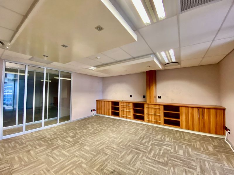 A vacant commercial office space featuring built-in wooden cabinetry, carpet tile flooring, a suspended ceiling with recessed lighting, and a glass partition wall.