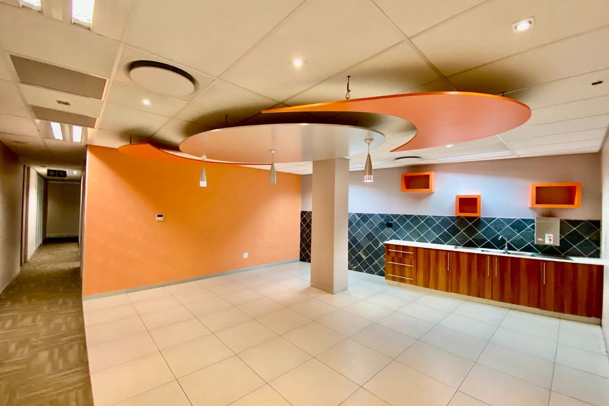 A spacious commercial kitchenette area featuring tiled flooring, built-in wooden cabinetry, a tiled backsplash, and a unique decorative suspended ceiling feature.
