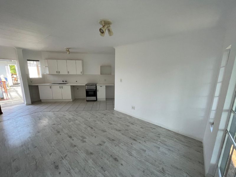 An open-plan living and kitchen area featuring laminate flooring, tiled kitchen zone, built-in cabinetry, and a freestanding stove, presented in a clean, vacant state.