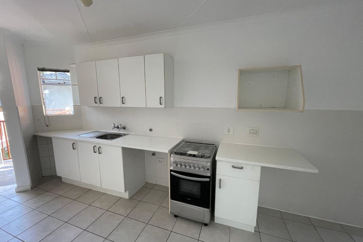 A functional kitchen featuring white cabinetry, tiled flooring, a stainless steel sink, and a freestanding stove, offering a clean and simple layout.