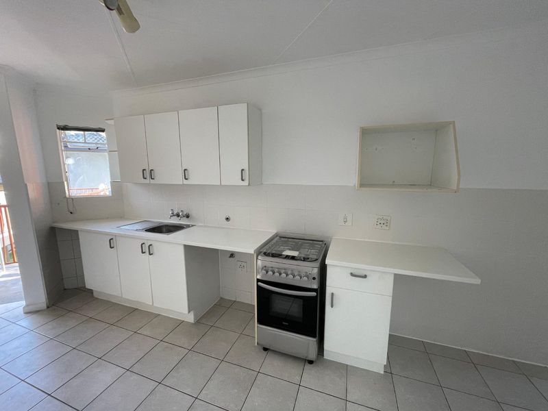 A functional kitchen featuring white cabinetry, tiled flooring, a stainless steel sink, and a freestanding stove, offering a clean and simple layout.