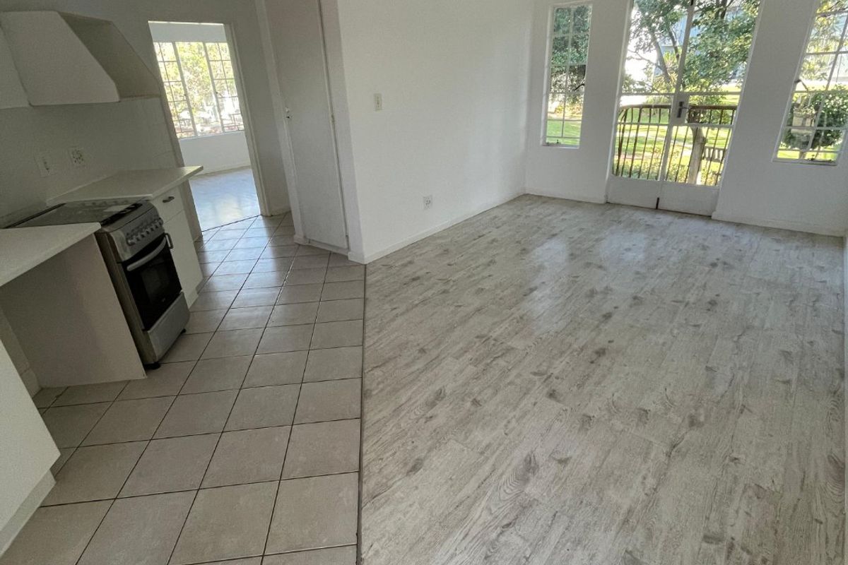 Open plan living area featuring a kitchen with a stove and extractor, transitioning from tiled to laminate flooring with access to a balcony.
