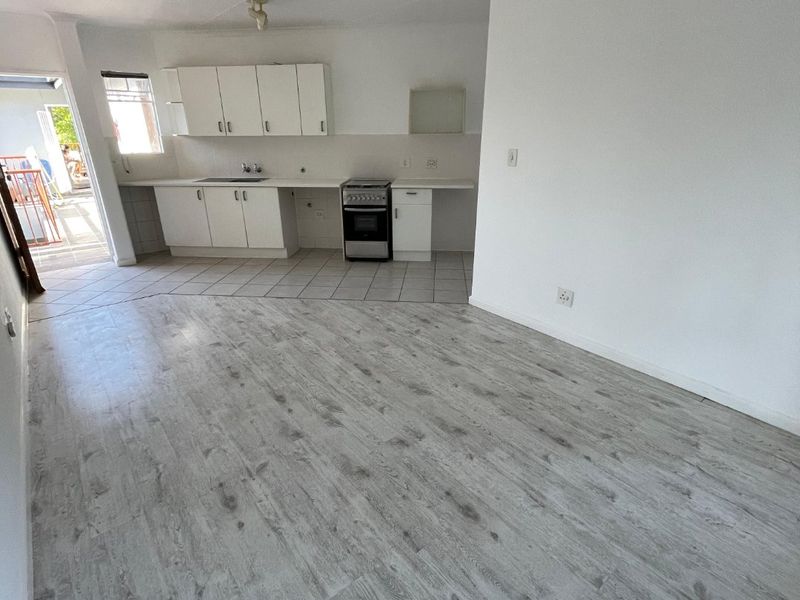 Open-plan living and kitchen area featuring light wood-look laminate flooring, tiled kitchen zone, built-in cabinetry, and a freestanding stove with direct outdoor access.