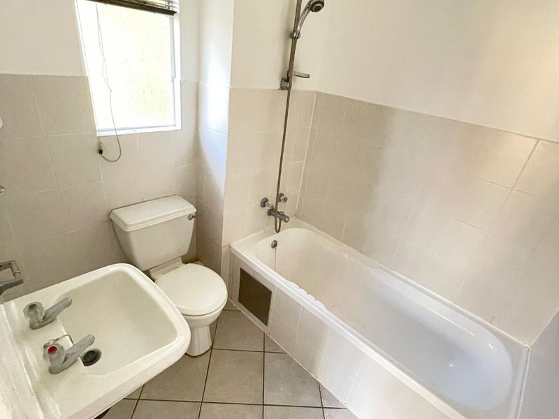 A functional bathroom featuring a bathtub with shower mixer, pedestal basin, and toilet, finished with neutral wall and floor tiles.