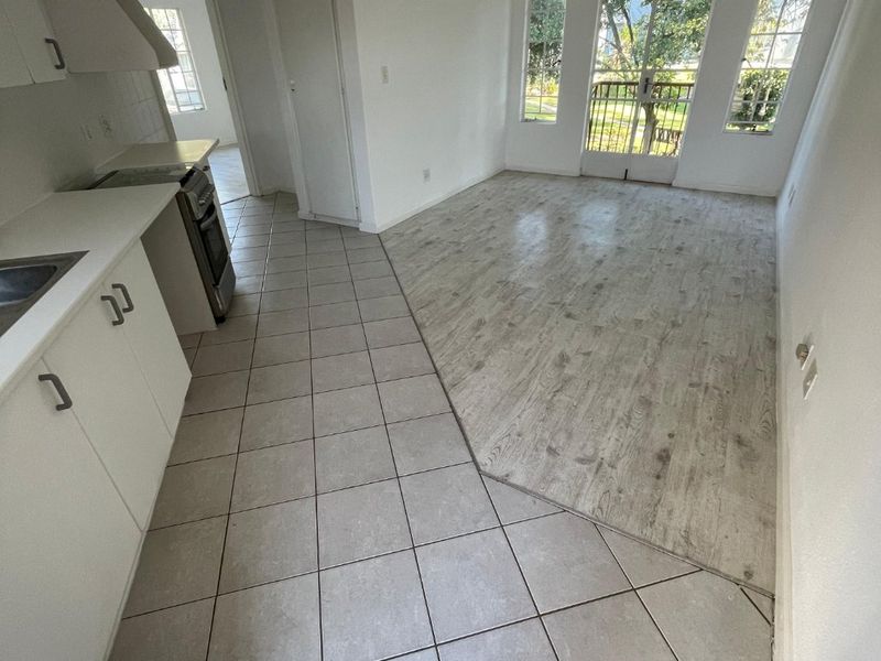 Open-plan kitchen and living area featuring a mix of tiled and laminate flooring, built-in cabinetry, and direct access to an outdoor balcony.