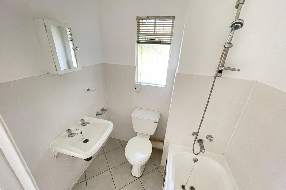 A functional bathroom featuring a wall-mounted basin, toilet, and bathtub with a shower mixer, finished with neutral wall and floor tiles.