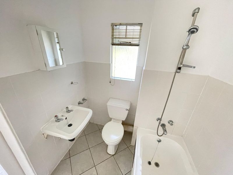 A functional bathroom featuring a wall-mounted basin, toilet, and bathtub with a shower mixer, finished with neutral wall and floor tiles.