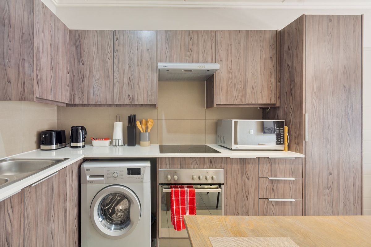 Modern kitchen featuring wood-grain laminate cabinetry, built-in oven, electric hob, extractor fan, and an integrated washing machine.