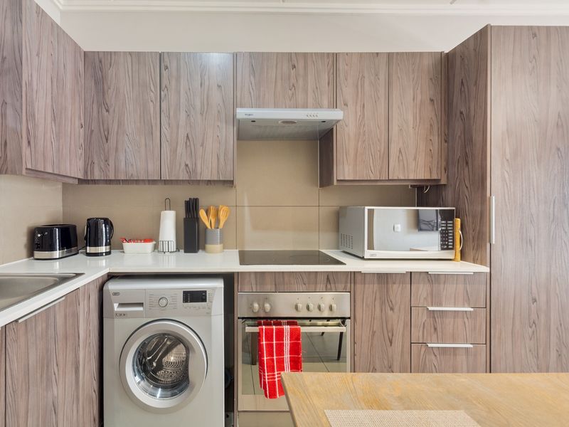 Modern kitchen featuring wood-grain laminate cabinetry, built-in oven, electric hob, extractor fan, and an integrated washing machine.