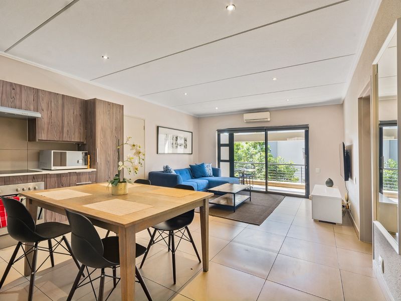 Modern open-plan living area featuring a well-appointed kitchen with built-in cabinetry, tiled floors, and seamless access to a private balcony through sliding glass doors.