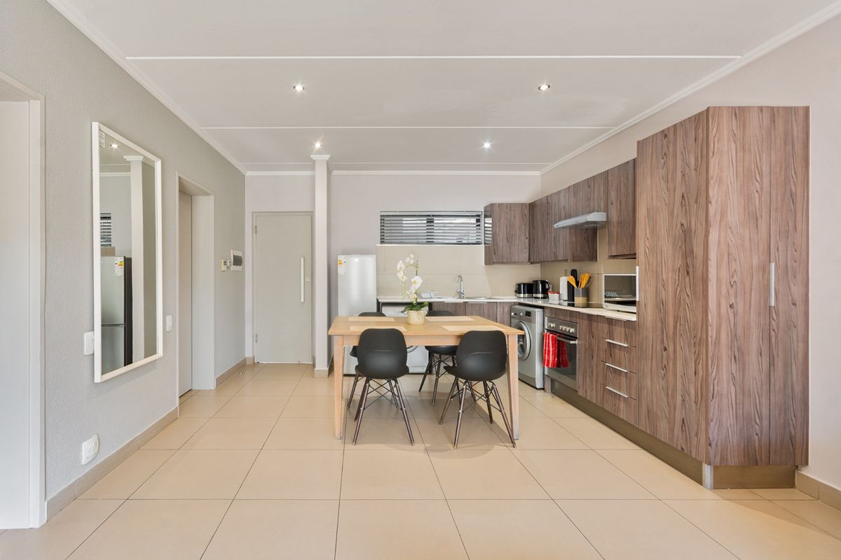 Modern open-plan kitchen and dining area featuring wood-grain cabinetry, integrated appliances, and neutral tiled flooring throughout.