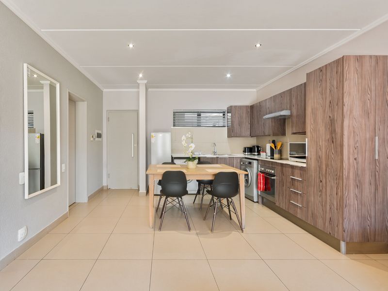 Modern open-plan kitchen and dining area featuring wood-grain cabinetry, integrated appliances, and neutral tiled flooring throughout.