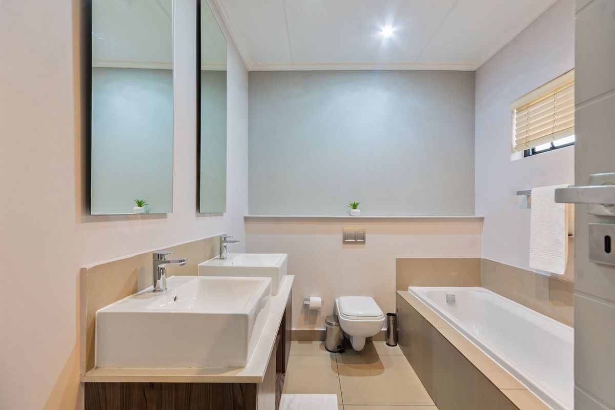 Modern bathroom featuring a double vanity, wall-mounted toilet, and a built-in bathtub with neutral tiling and clean finishes.